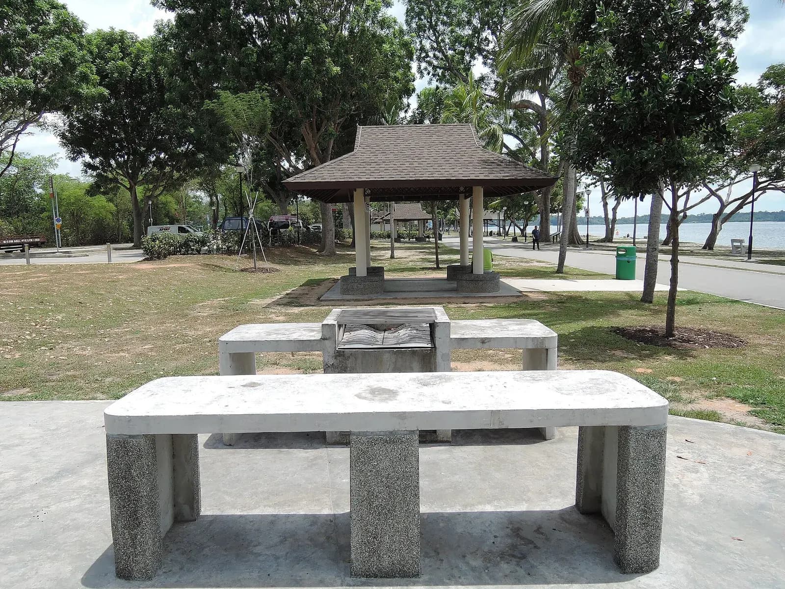 Concrete BBQ pit with stone benches at Changi Beach Park, with a shelter and the sea behind