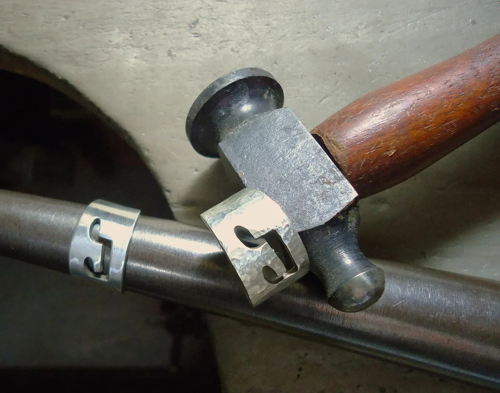 Two handmade silver rings on a steel ring mandrel beside a small ball-pein hammer