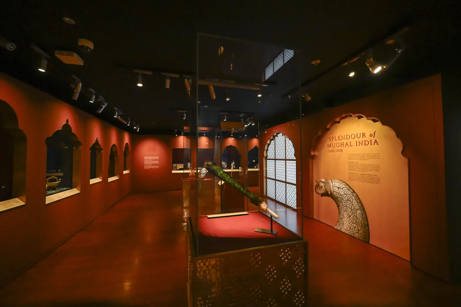 The Splendour of Mughal India gallery: a deep red wall with a scalloped ochre title arch and pierced screens