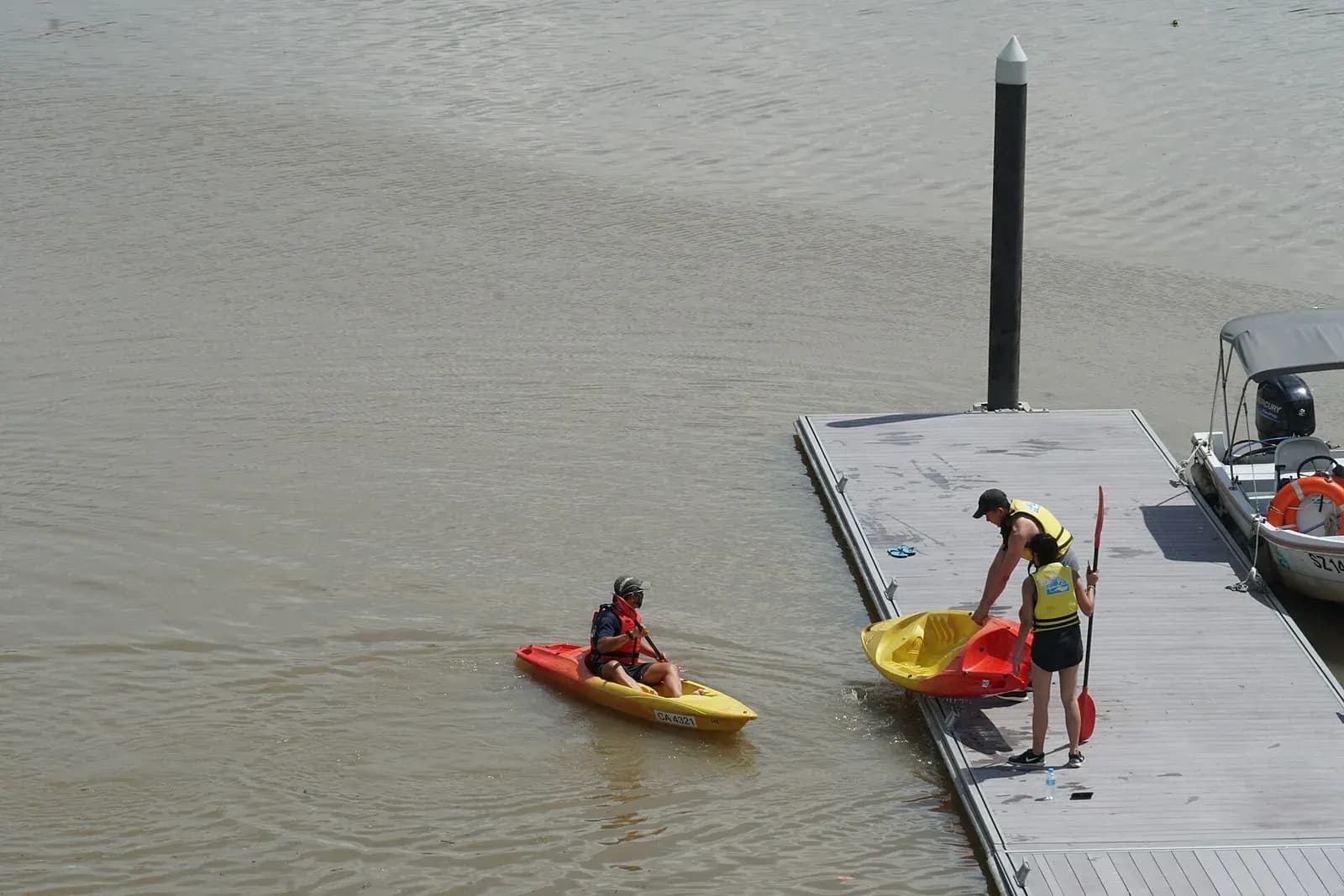 Beginners in life jackets launching sit-on-top kayaks from a pontoon at Jurong Lake, Singapore