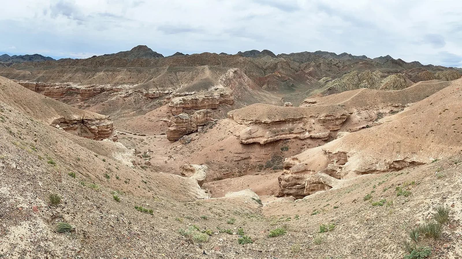 Panorama of layered red and sandy rock formations in Charyn Canyon under a cloudy sky